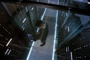 Top View Through the Glass of IT Engineer Working with Laptop in Data Center Full of  Active Rack Servers.